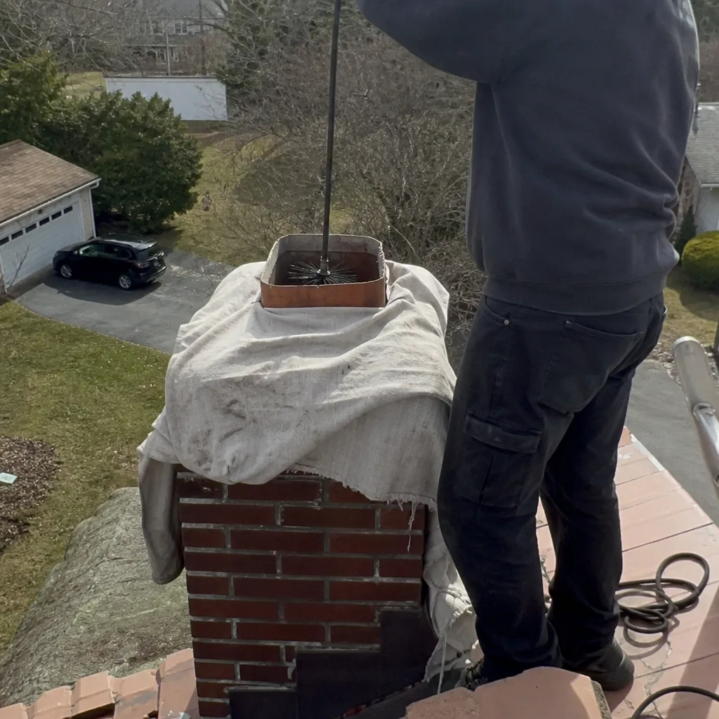 Professional chimney sweep cleaning a residential brick chimney flue from the roof